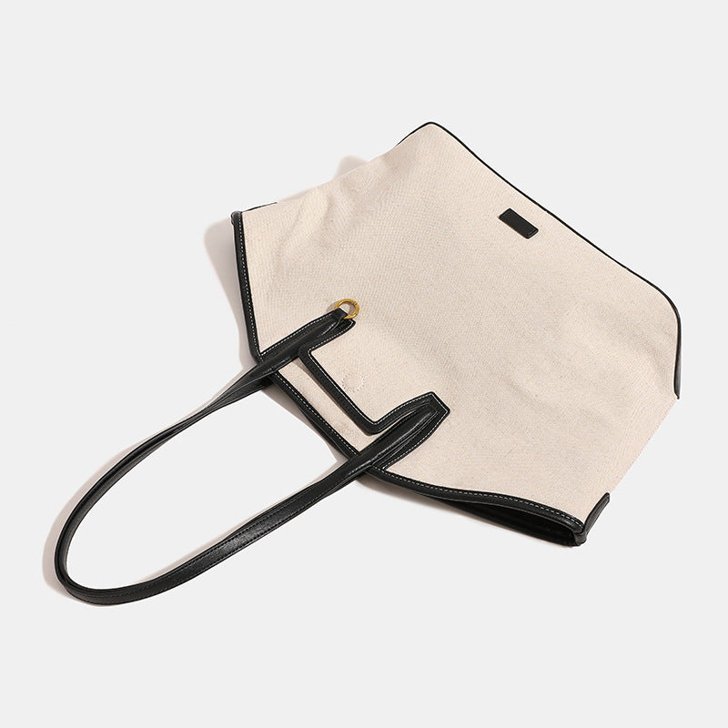 Trapezförmige Tote-Bag aus cremefarbenem Canvas mit schwarzem Besatz in Lederoptik, zwei Schulterriemen und goldfarbenen Ringbeschlägen, Detailansicht