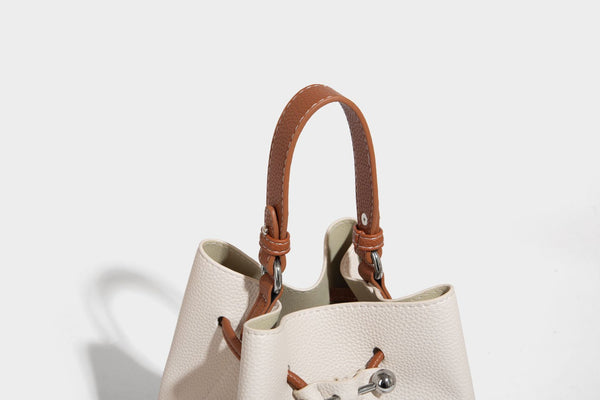 Small two-tone pebbled drawstring bucket bag with tan contrast base, metal toggle hardware, short top handle, and detachable