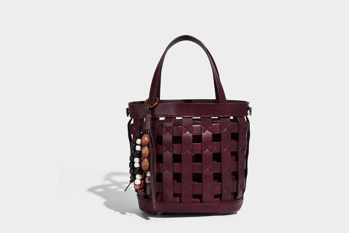 Small woven lattice bucket bag in brown leather-look finish with beaded tassel charm, dual top handles, and detachable