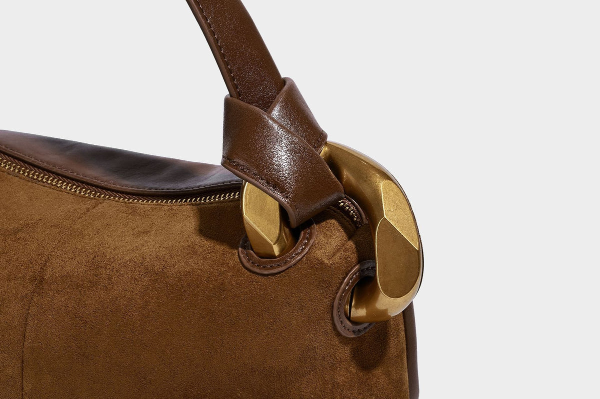 Kompakte Boston-Schultertasche in warmem Braun in Wildlederoptik mit glattem dunkelbraunem Besatz, übergroßen goldfarbenen Ringelementen und Reißverschluss oben