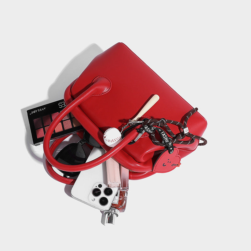 Small structured shell top-handle bag in red with heart charm and braided cord detail, smooth leather-look finish, detail