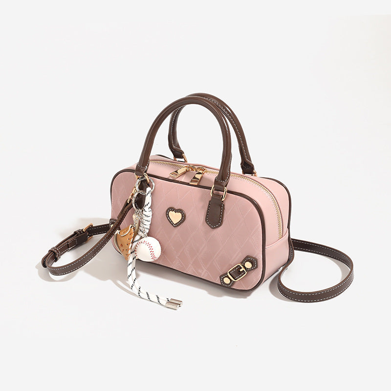 Blush pink quilted bowling barrel bag with dark brown leather-look trim and handles, baseball bat and ball charm, gold-tone