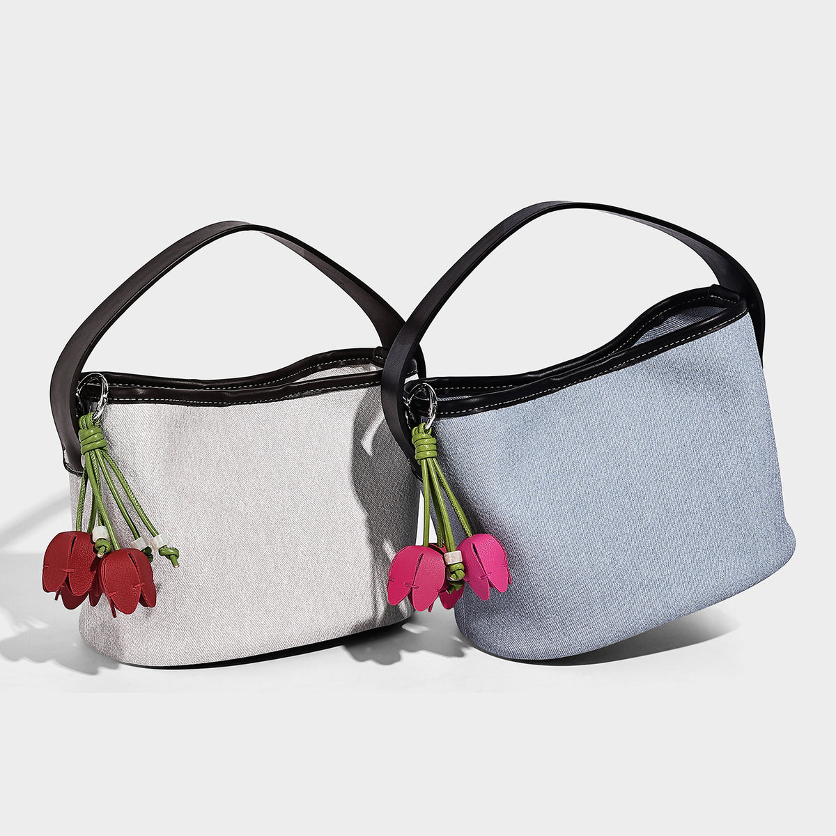 Small denim-look bucket bag with black leather-look trim, pink tulip flower charm, and adjustable crossbody strap, detail