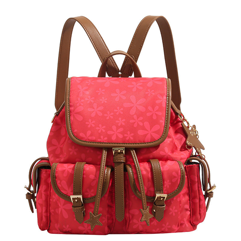 Red floral-print backpack handbag with brown leather-look trim, dual front buckle pockets, star charms, and gold-tone, detail