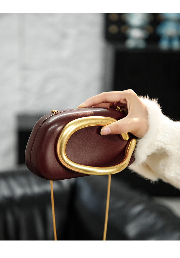 Kleine Crossbody-Clutch in abgerundeter Rechteckform mit übergroßem poliertem C-förmigem Goldhenkel und schmalem Goldkettenriemen, Detailansicht