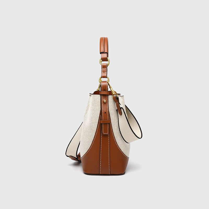 Cream canvas and tan leather-look bucket bag with arched top handle, wide detachable shoulder strap, and gold-tone hardware