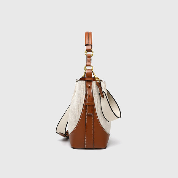 Cream canvas and tan leather-look bucket bag with arched top handle, wide detachable shoulder strap, and gold-tone hardware