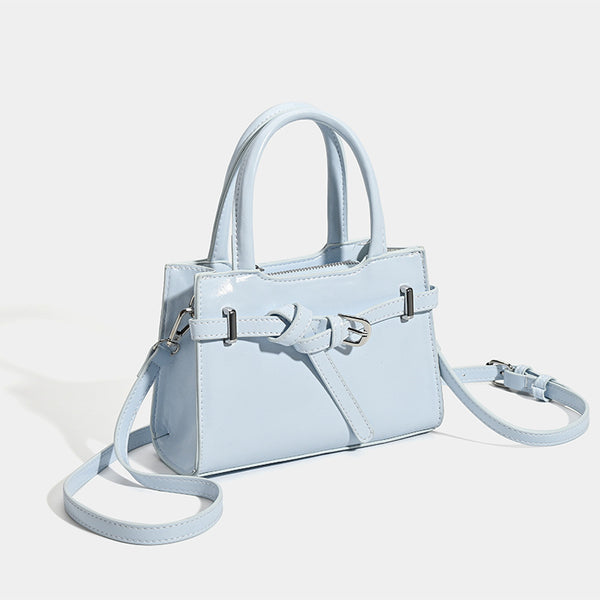 Small structured trapezoid mini top-handle bag with front belt-knot buckle detail and glossy leather-look finish, detail view