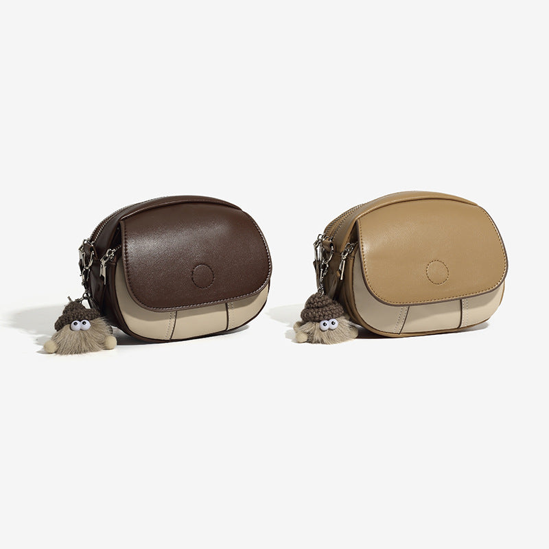 Compact two-tone oval crossbody bag in tan and cream leather-look finish with silver hardware and plush charm, detail view 2