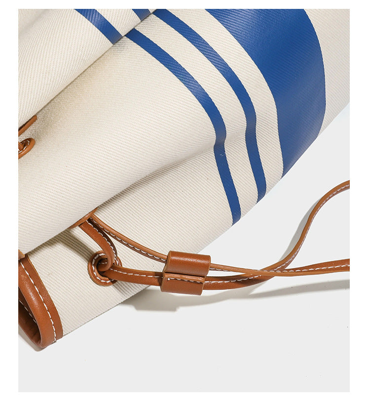 Large cream and navy striped canvas bucket tote bag with tan leather-look trim, drawstring closure, and double shoulder
