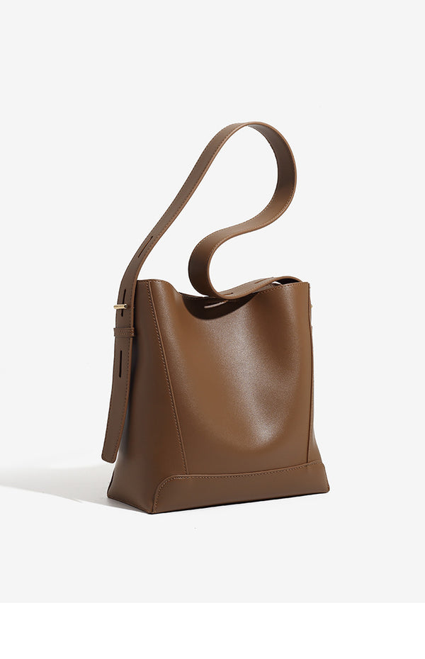 Structured smooth leather-look bucket shoulder bag with long adjustable strap and gold-tone buckle hardware in brown, detail