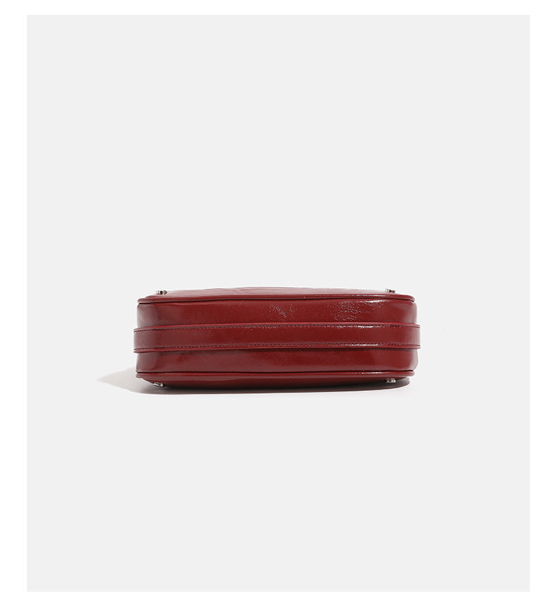Compact crescent hobo shoulder bag in glossy burgundy leather-look finish with silver chain strap, red and green bead tassel