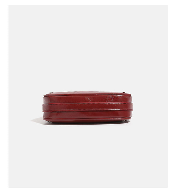 Compact crescent hobo shoulder bag in glossy burgundy leather-look finish with silver chain strap, red and green bead tassel