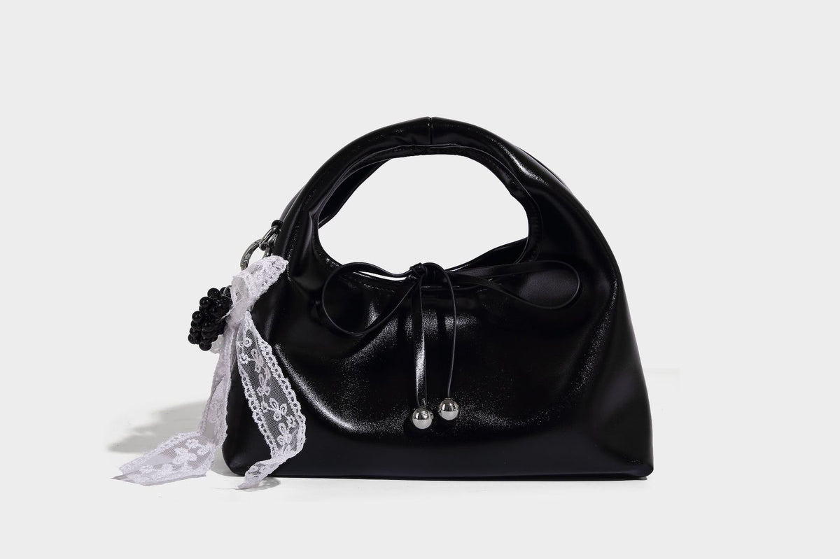 Kleine kuppelförmige Henkeltasche in glänzender Lederoptik mit Kordelzugverschluss, weißem Spitzen-Schleifenanhänger und silberfarbenen Metallbeschlägen