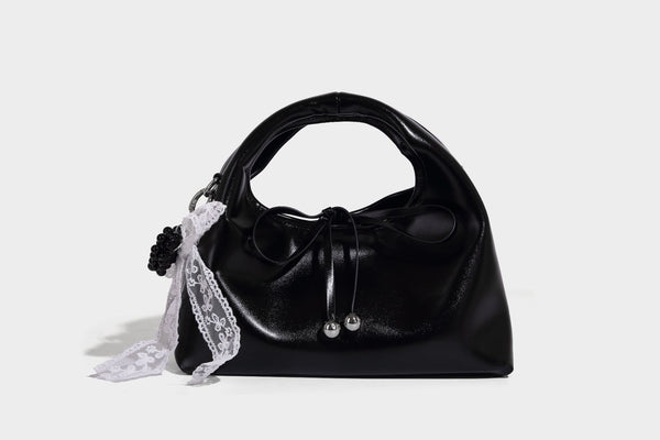 Kleine kuppelförmige Henkeltasche in glänzender Lederoptik mit Kordelzugverschluss, weißem Spitzen-Schleifenanhänger und silberfarbenen Metallbeschlägen
