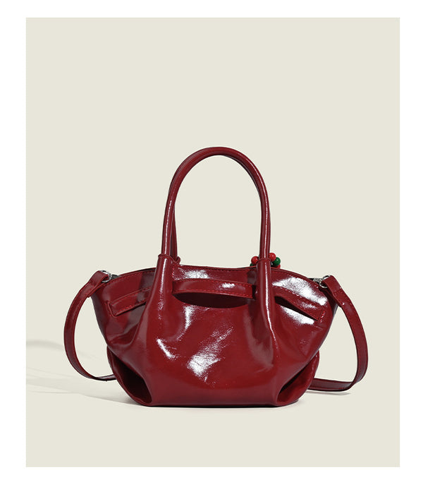 Small structured red glossy PU handbag with bow-and-bead charm, dual top handles, and detachable crossbody strap, detail view