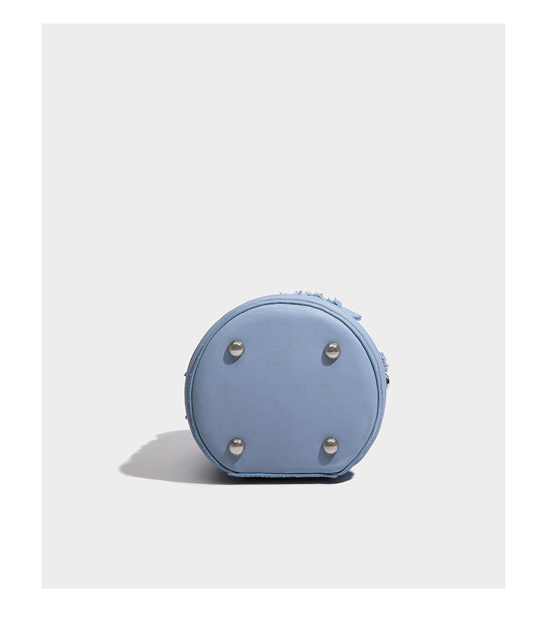 Mini cylindrical barrel bucket bag in denim patchwork with frayed edges, smooth leather-look trim, zip-around top closure