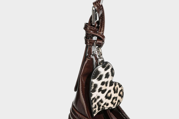 Glänzende dunkelbraune, lässig geschnittene Hobo-Schultertasche mit Riemendetail mit silberfarbenen Ösen, Reißverschlussfach auf der Vorderseite und Herz mit Leopardenmuster