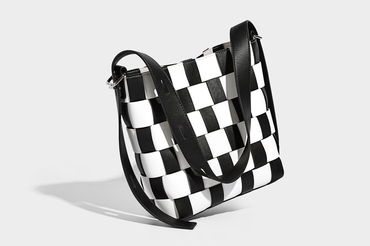 Hand-woven black-and-white checkerboard bucket bag with smooth black trim, silver-tone ring hardware, and adjustable