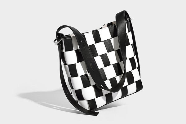 Hand-woven black-and-white checkerboard bucket bag with smooth black trim, silver-tone ring hardware, and adjustable