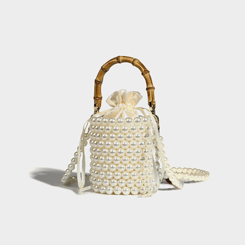 Small cylindrical bucket bag with glossy faux-pearl bead exterior, bamboo arched top handle, satin drawstring closure, and