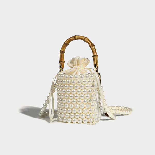 Small cylindrical bucket bag with glossy faux-pearl bead exterior, bamboo arched top handle, satin drawstring closure, and