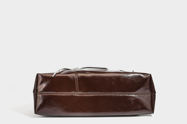 Weich fallende Hobo-Schultertasche in glänzender Lederoptik mit silberfarbenen Ösen zum Schnüren und Schleifenband auf der Vorderseite, Detailansicht