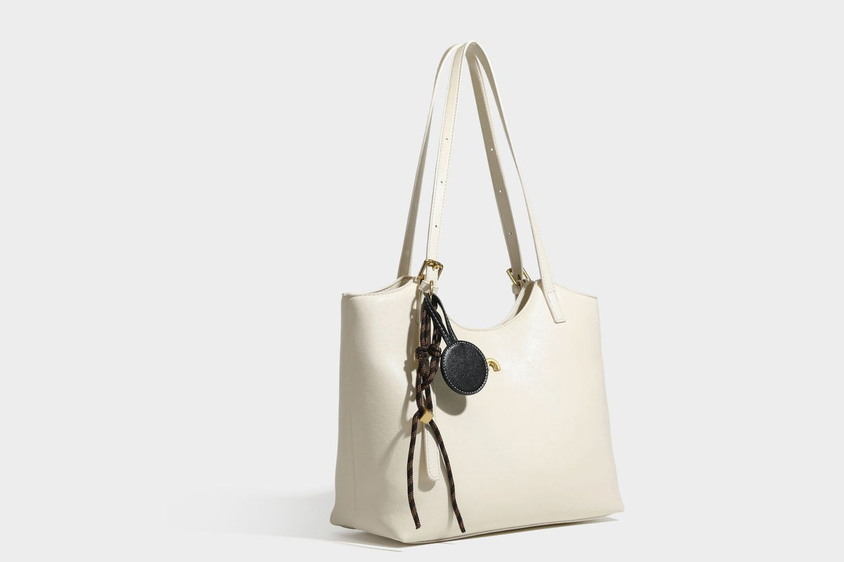 Structured smooth leather-look tote bag with long shoulder strap, gold-tone hardware, and hanging tassel-coin charm, detail
