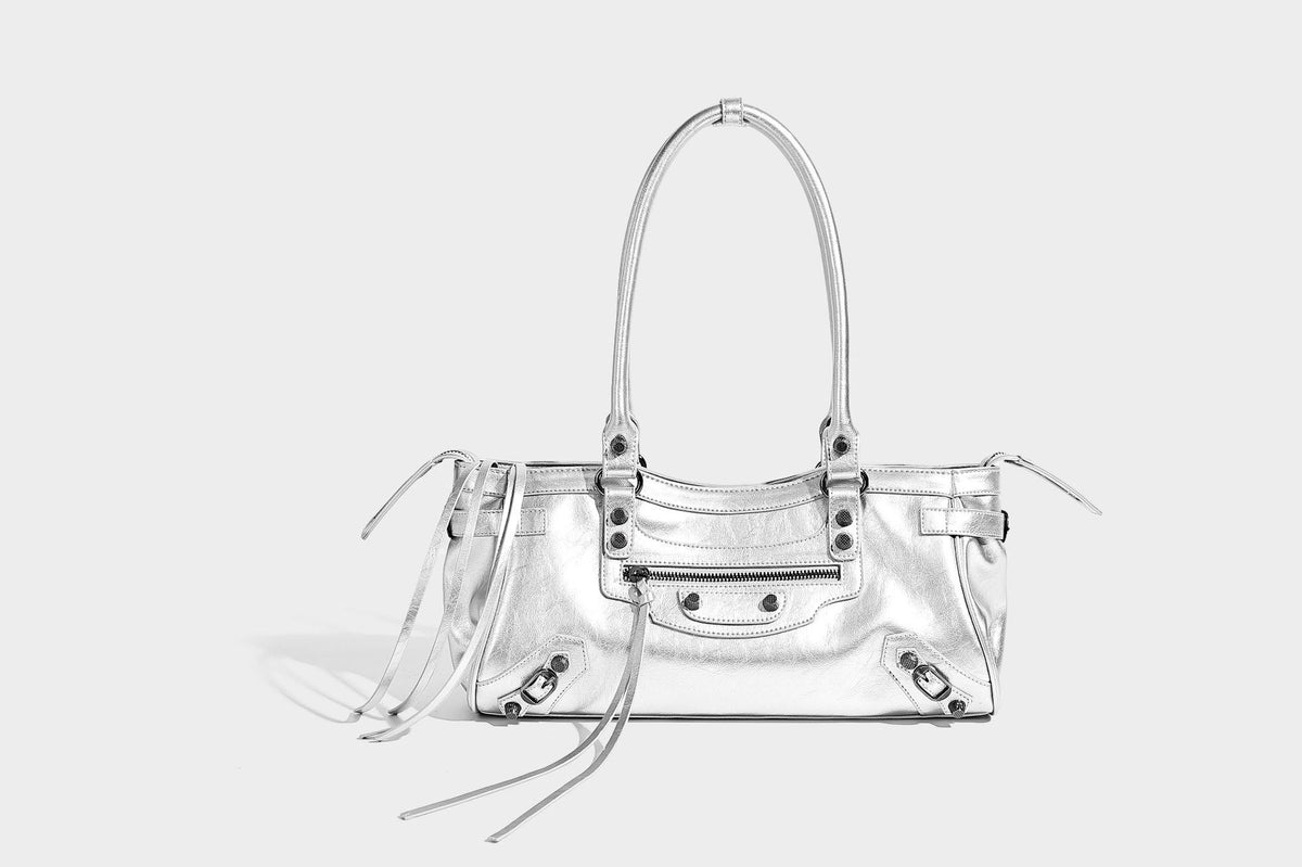 Längliche Schultertasche in Zylinderform mit glänzender Lederoptik, silberfarbenen Nietenbeschlägen, seitlichen Quasten und mehreren außenliegenden Reißverschlüssen