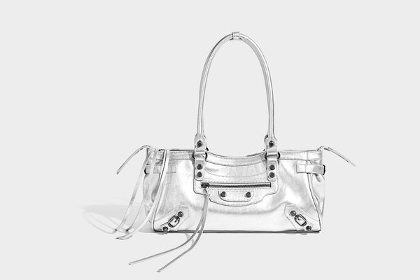 Längliche Schultertasche in Zylinderform mit glänzender Lederoptik, silberfarbenen Nietenbeschlägen, seitlichen Quasten und mehreren außenliegenden Reißverschlüssen