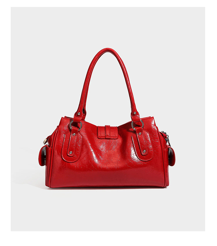 Glänzende, geknautschte Barrel-Satchel mit zwei oberen Tragegriffen, vorderem Klappen-Riemen-Panel, Ring- und Nietenbeschlägen sowie einem abnehmbaren