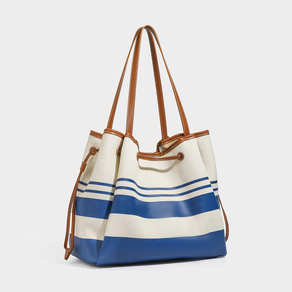Large cream and navy striped canvas bucket tote bag with tan leather-look trim, drawstring closure, and double shoulder
