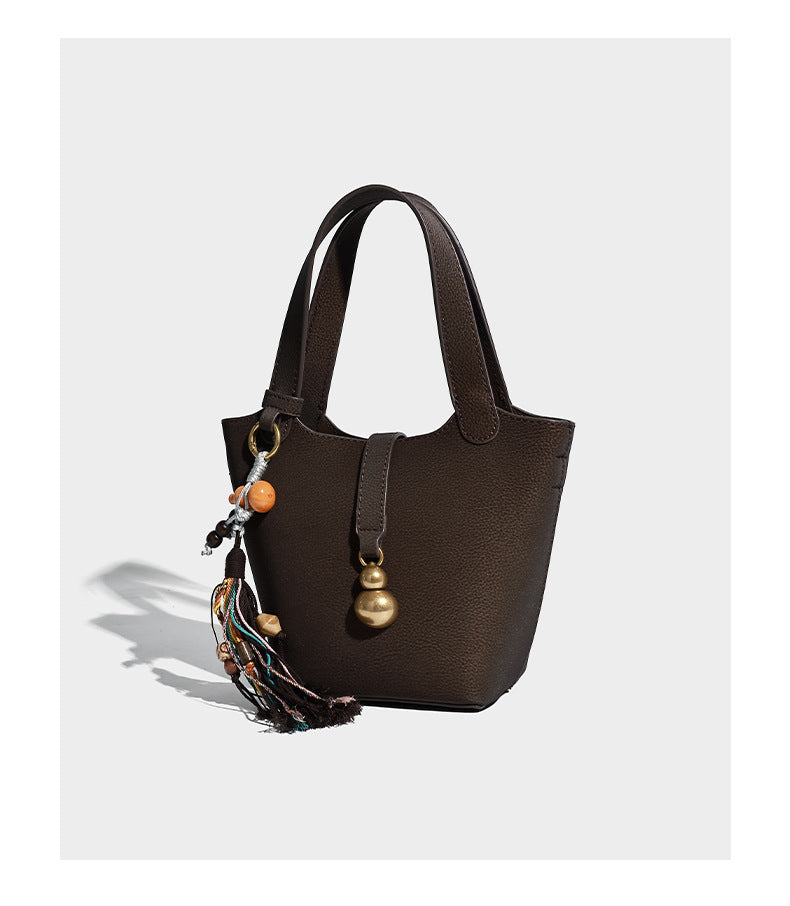 Kleine matte Beuteltasche mit genarbter Oberfläche, antikgoldfarbenen Ringbeschlägen, Perlen- und Quastenanhänger, kurzen Tragegriffen oben und
