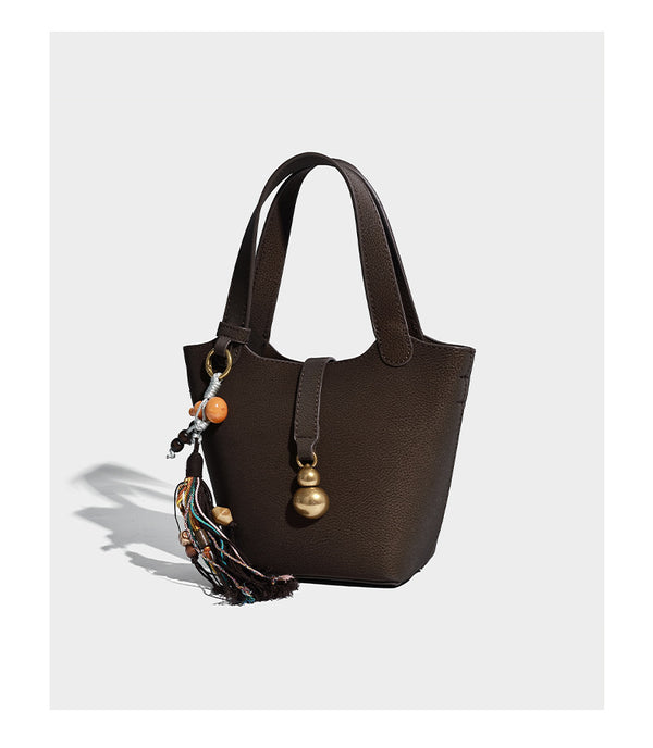 Kleine matte Beuteltasche mit genarbter Oberfläche, antikgoldfarbenen Ringbeschlägen, Perlen- und Quastenanhänger, kurzen Tragegriffen oben und