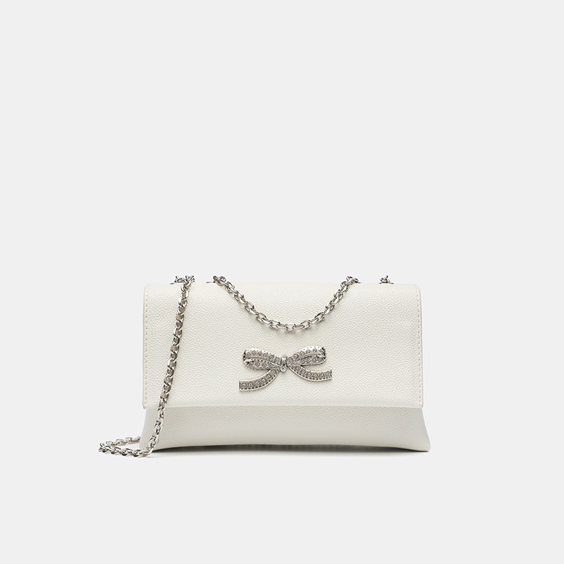 Structured rectangular flap crossbody bag with rhinestone bow and silver chain strap in pebbled finish, detail view 7