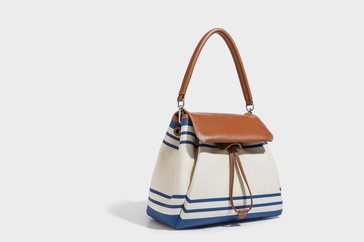Cream canvas bucket bag with blue horizontal stripes, tan leather-look flap and trim, drawstring closure, silver-tone, detail