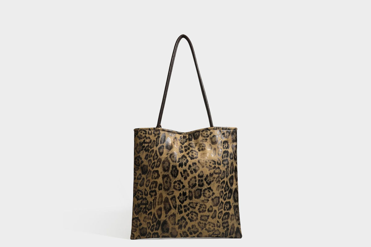Large leopard print shoulder tote bag in tan and brown with slim dark straps and dangling beaded charm hardware, detail view
