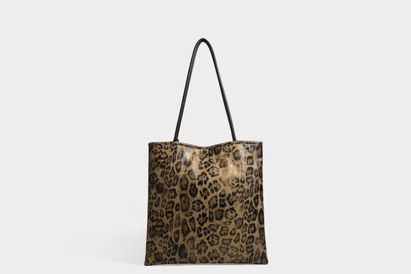 Large leopard print shoulder tote bag in tan and brown with slim dark straps and dangling beaded charm hardware, detail view