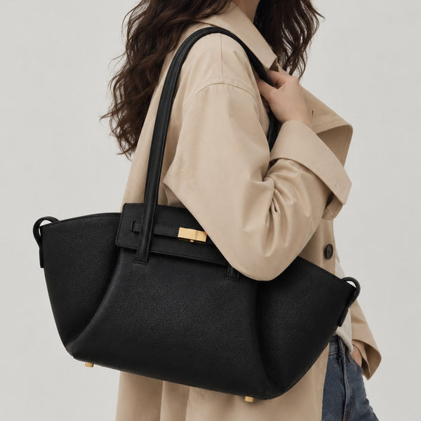 Black pebbled trapezoid tote bag with gold turn-lock hardware and double top handles, detail view 3