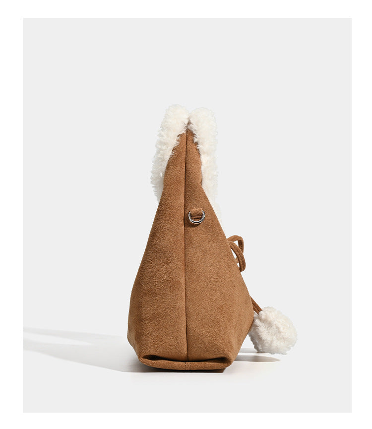 Trapezförmige Tasche in Karamellbraun mit Wildlederoptik, ovalem Henkel aus weißem Kunstfell, Kordelverschluss mit Pompons und abnehmbarem Schulterriemen