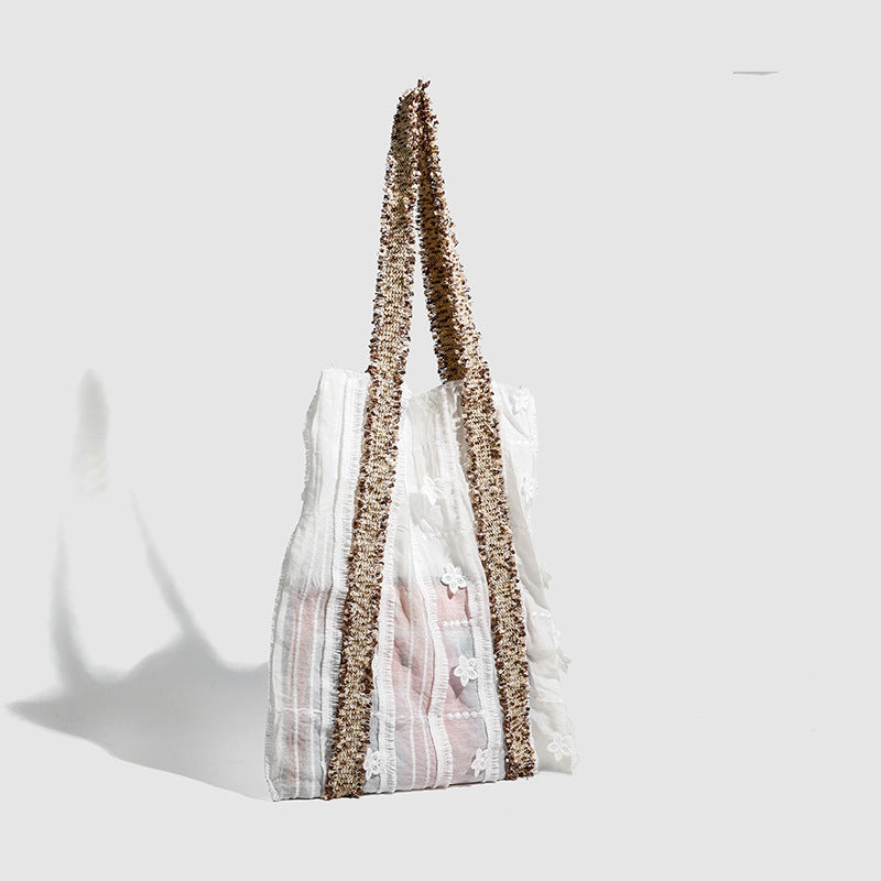 Offwhitefarbener weicher Canvas-Schultershopper mit offenen Seiten und braun-goldfarbenen Jacquard-Gurtbändern mit Blumenmuster, lässig rechteckige Form, Detailansicht