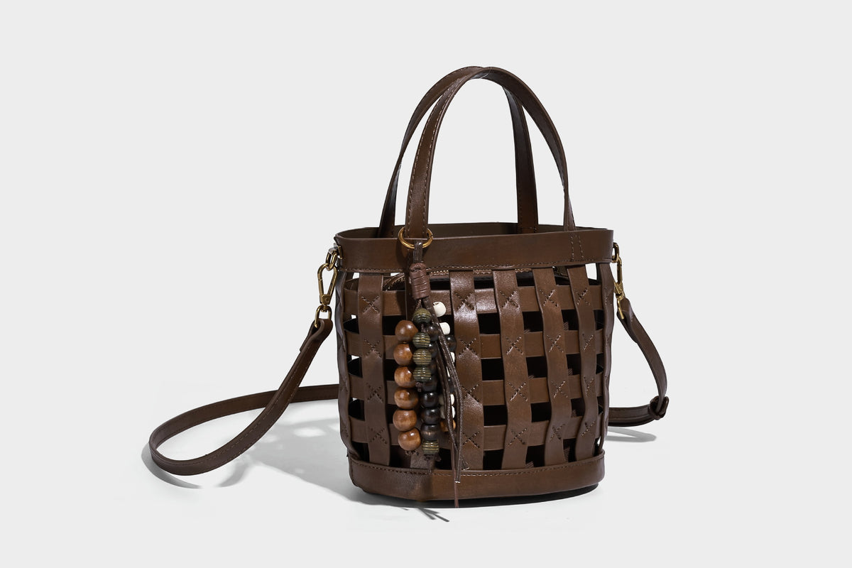 Small woven lattice bucket bag in brown leather-look finish with beaded tassel charm, dual top handles, and detachable