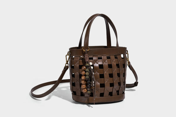 Small woven lattice bucket bag in brown leather-look finish with beaded tassel charm, dual top handles, and detachable