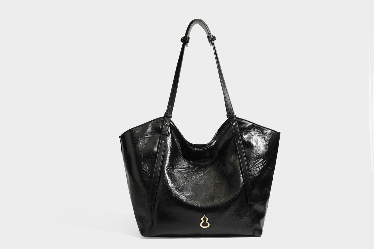 Große, glänzende Tote-Bag aus schwarzem Lederimitat mit geknitterter Optik, lässig fallender Trapezsilhouette, zwei Schulterriemen und goldfarbenen