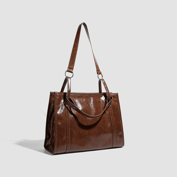 Large structured glossy leather-look tote bag with dual top handles and long shoulder strap in burnished brown, detail view 2