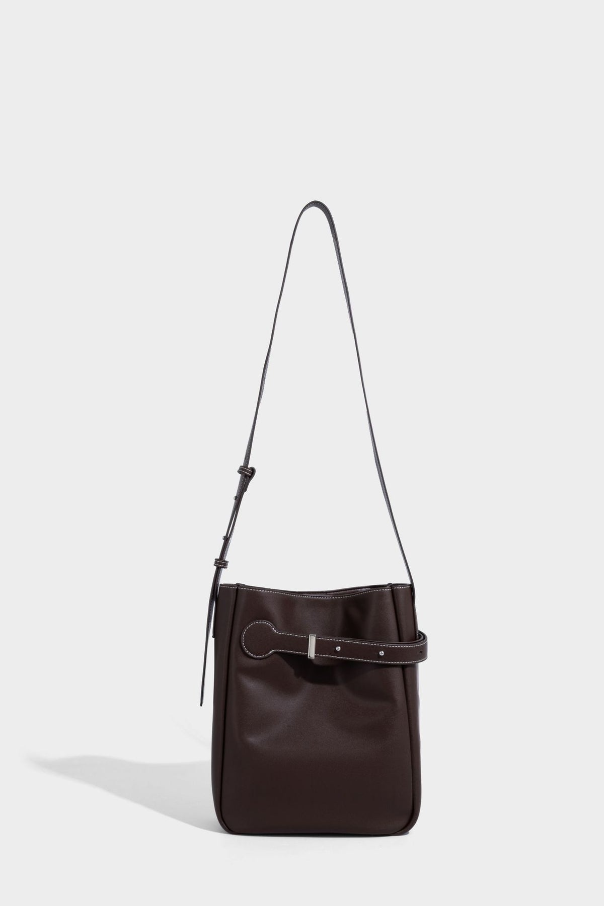 Structured dark brown leather-look bucket bag with white contrast stitching, front wraparound belt buckle strap, and long