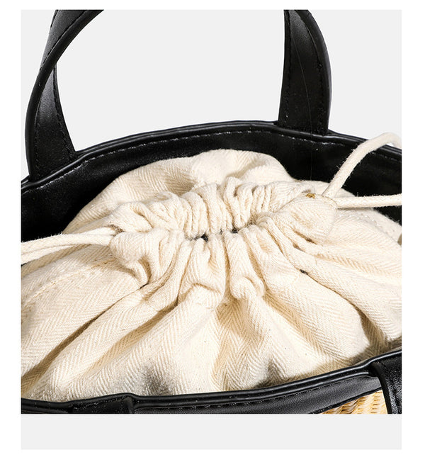 Kleine geflochtene Bucket Bag aus Stroh mit schwarzem Besatz in Lederoptik, zwei oberen Tragegriffen, cremefarbenem Futter mit Kordelzug und seitlichen Kordelverschlüssen