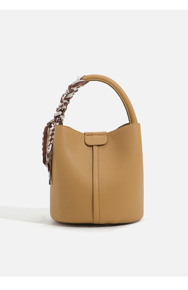 Pebbled leather-look bucket bag with checkered scarf-wrapped top handle, flap tab closure, gold-tone hardware, and matching