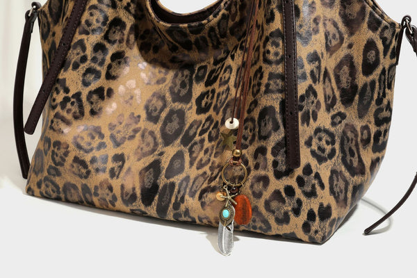 Slouchy leopard-print shoulder tote bag in tan and brown with long double straps, side tie straps, and dangling charm, detail