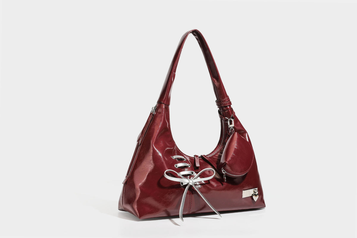 Weich fallende Hobo-Schultertasche in glänzender Lederoptik mit silberfarbenen Ösen zum Schnüren und Schleifenband auf der Vorderseite, Detailansicht